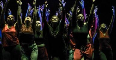 Dancers with lifted hands look upward during performance